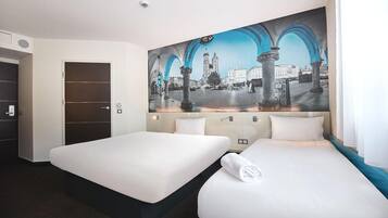 Habitación de hotel con dos camas, un mural de paisaje urbano en la pared y una puerta a la izquierda.