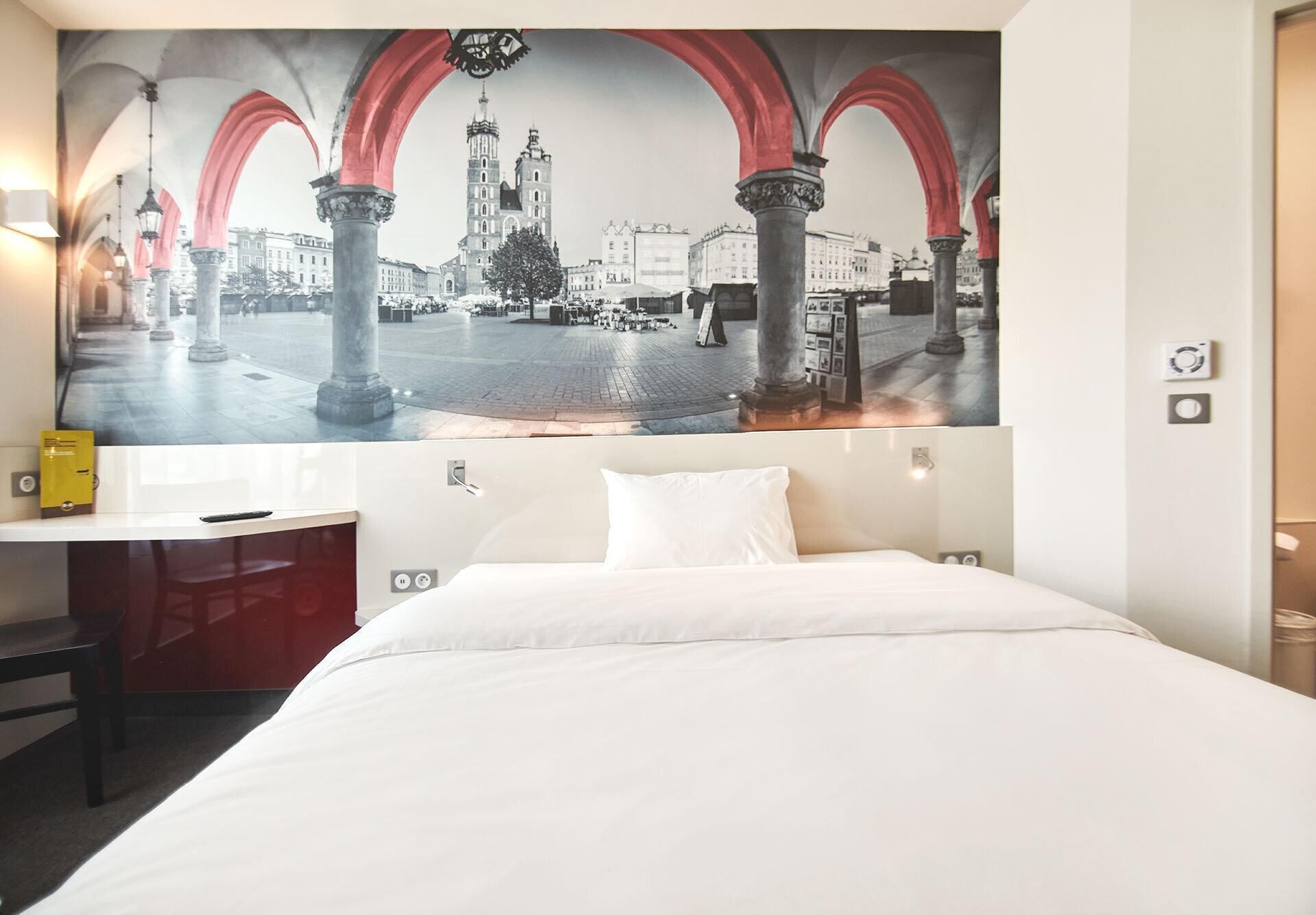 A hotel room with a bed, a desk, and a large cityscape mural on the wall.