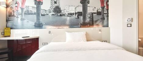 A hotel room with a bed, a desk, and a large cityscape mural on the wall.