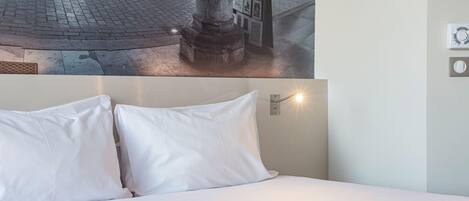 A hotel room with a bed, a wall-mounted light, and a poster of a street scene.