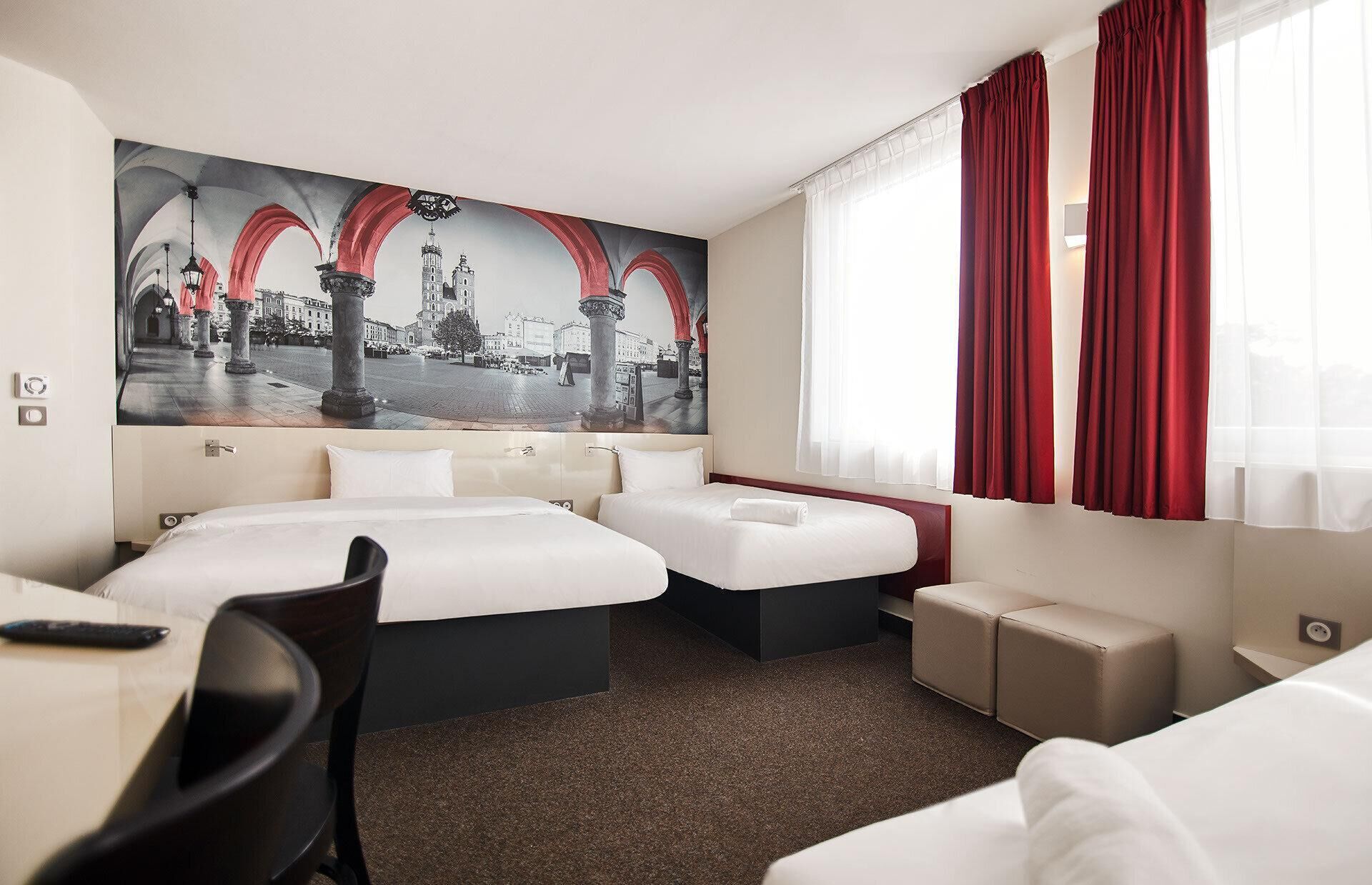 Habitación de hotel con dos camas, un escritorio y un cuadro grande con una vista panorámica de la ciudad.
