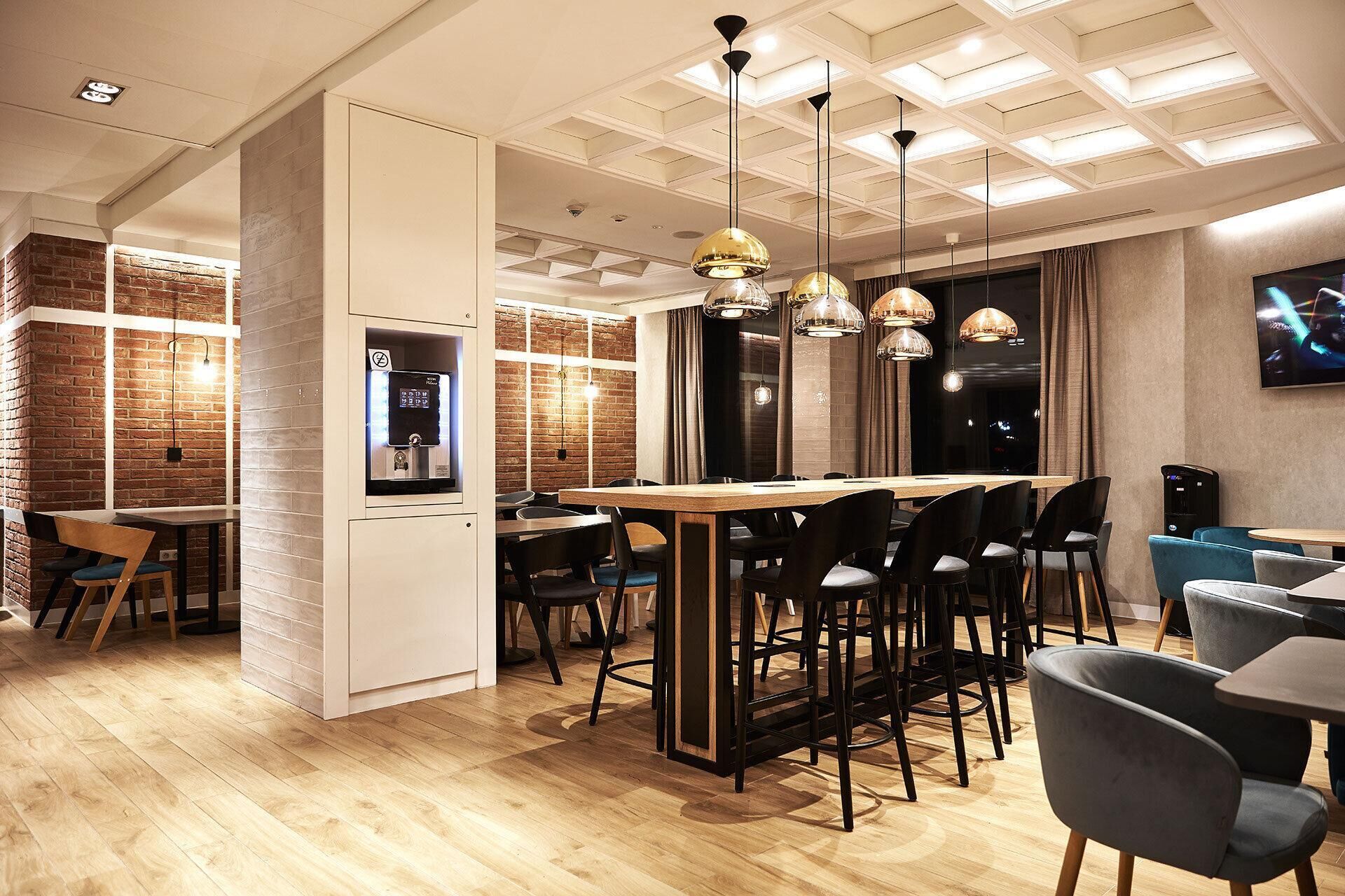 Un restaurante moderno con pared de ladrillo, mesas de madera y sillas negras.
