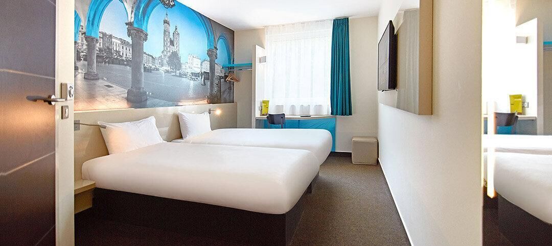 Quarto de hotel com uma cama grande, uma escrivaninha e um mural de uma paisagem urbana.