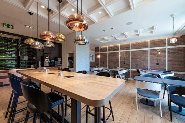 A modern restaurant with a long wooden bar, black and white chairs, and hanging copper pendant lights.