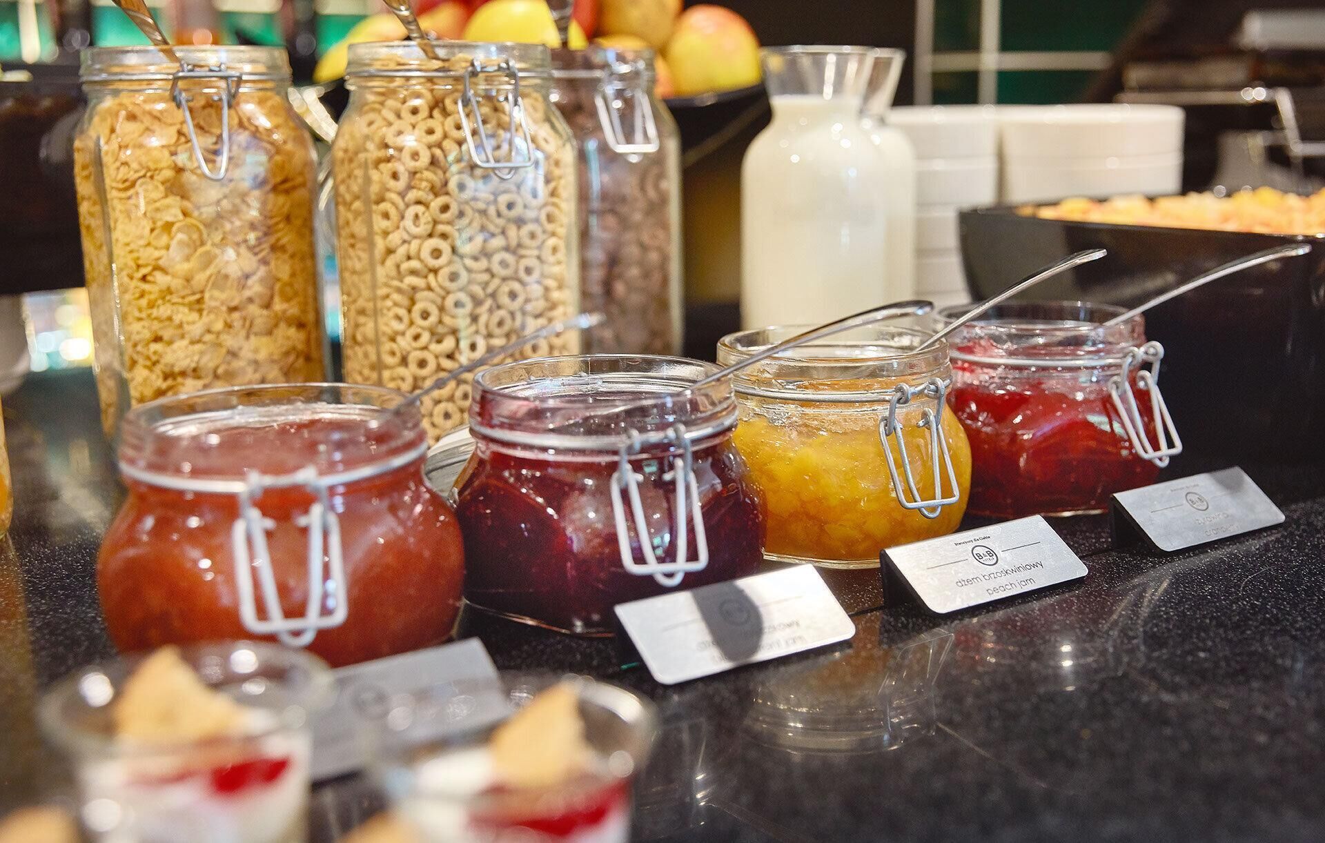 A buffet with various food items including cereal, fruit preserves, and a milk jug.