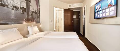 A hotel room with two beds, a large TV on the wall, and a mural of a cityscape.