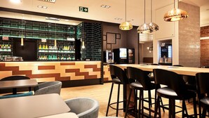 Een moderne bar met een toonbank, barstoelen en een zithoek met tafels en stoelen.