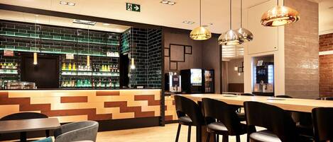 Un área de bar moderna con barra, taburetes y un espacio de estar con mesas y sillas.
