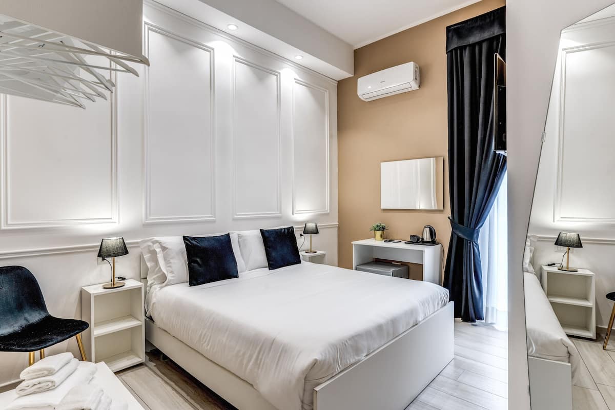 A modern hotel room with a large bed, bedside tables, a desk, and a wardrobe.