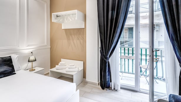 A hotel room with a bed, bedside table, lamp, and a small seating area with towels. - RAGGIO DI SOLE - ATAROOMS Collection (Naples)