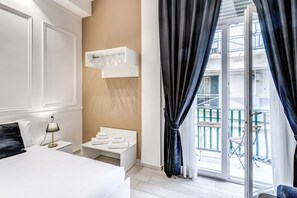 Habitación de hotel con cama, mesita de noche, lámpara y una pequeña zona de estar con toallas.