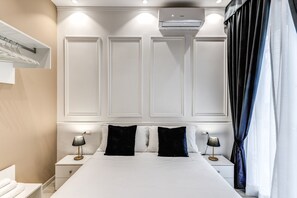Una habitación de hotel con una cama grande, dos mesitas de noche con lámparas, aire acondicionado montado en la pared y un perchero.