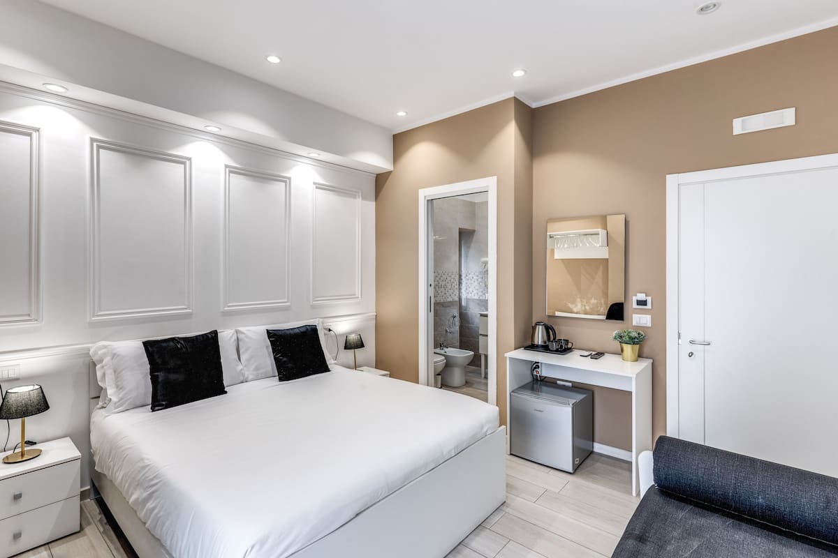 A modern bedroom with a large bed, bedside tables, a desk, and a wardrobe.