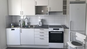 A modern kitchen with white cabinets, a built-in oven, a coffee maker, and a dishwasher. - Sjöhuset (Ellos)