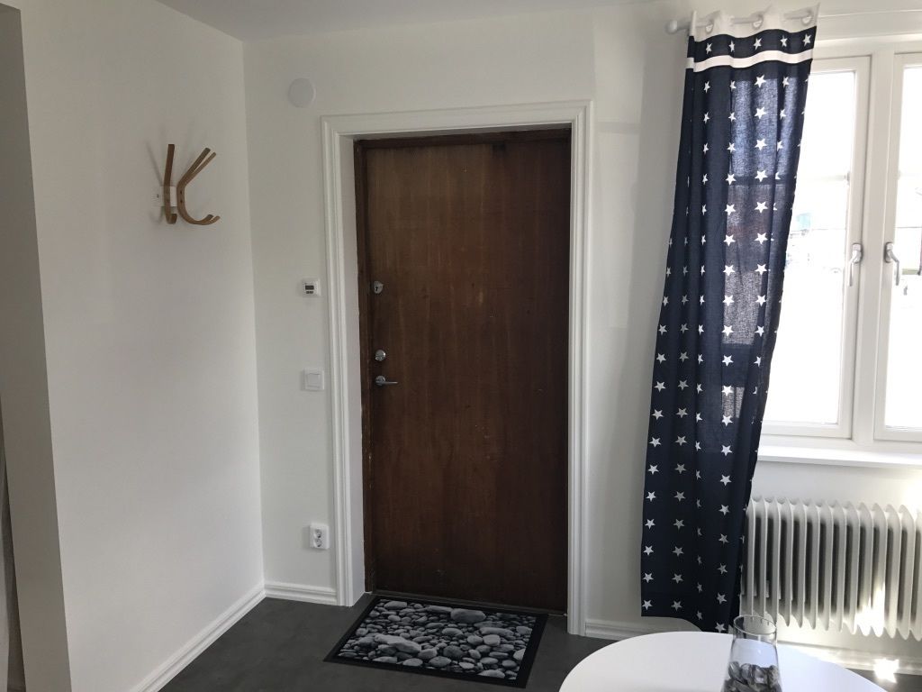 A room with a wooden door, a star-patterned curtain, a radiator, and a doormat with stones.