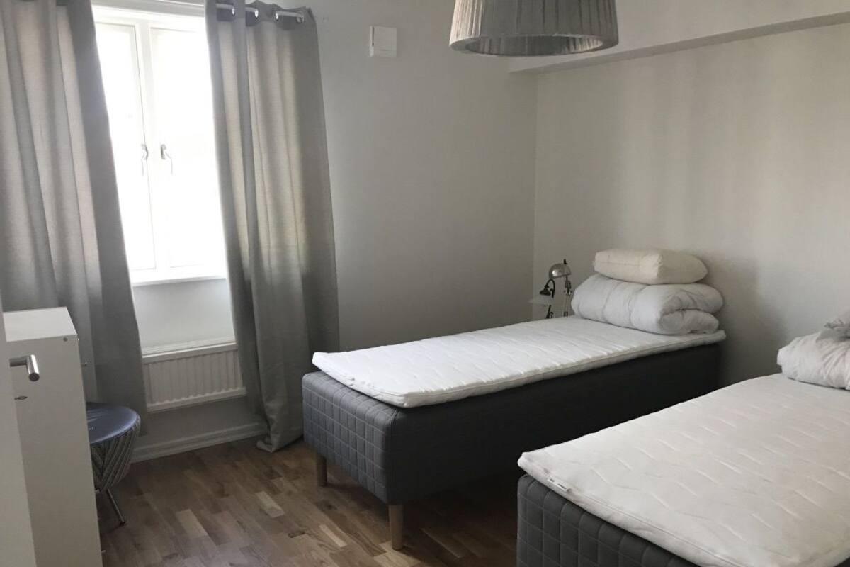 A bedroom with two single beds, a bedside table, a lamp, and a window with curtains.