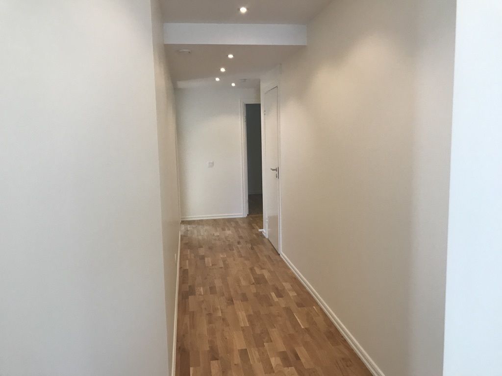 Een smalle gang met houten vloer en witte wanden.