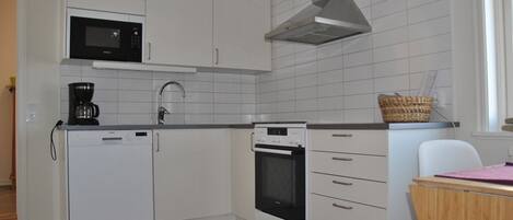 Una cocina compacta con gabinetes blancos, microondas, cafetera y estufa.
