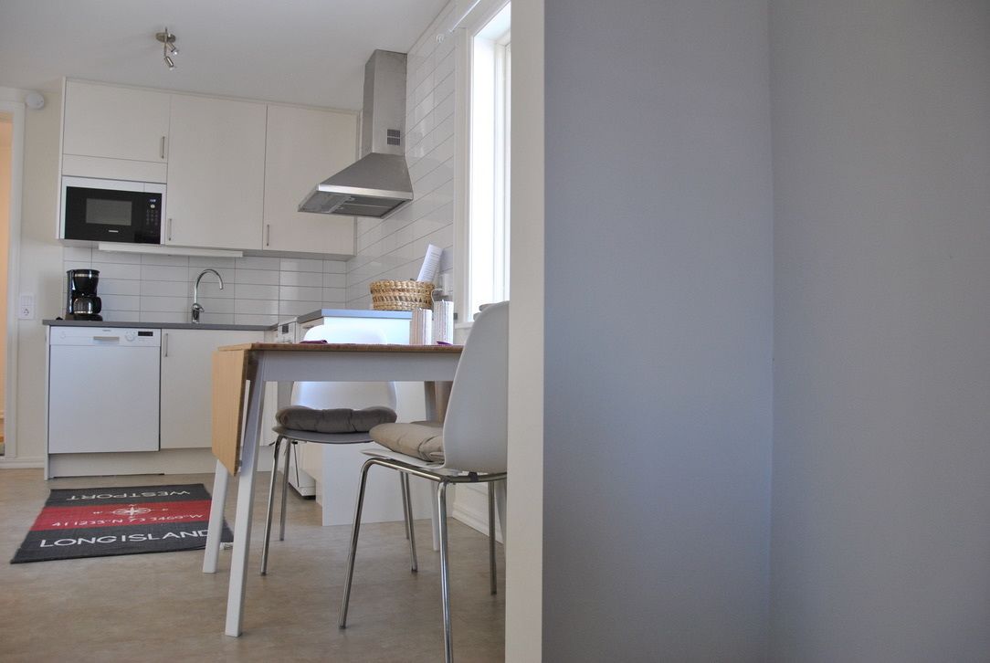 A compact kitchen with white cabinets, a microwave, a coffee maker, and a dining area with a chair and table.