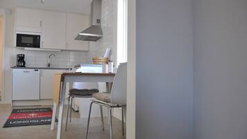 A compact kitchen with white cabinets, a microwave, a coffee maker, and a dining area with a chair and table.