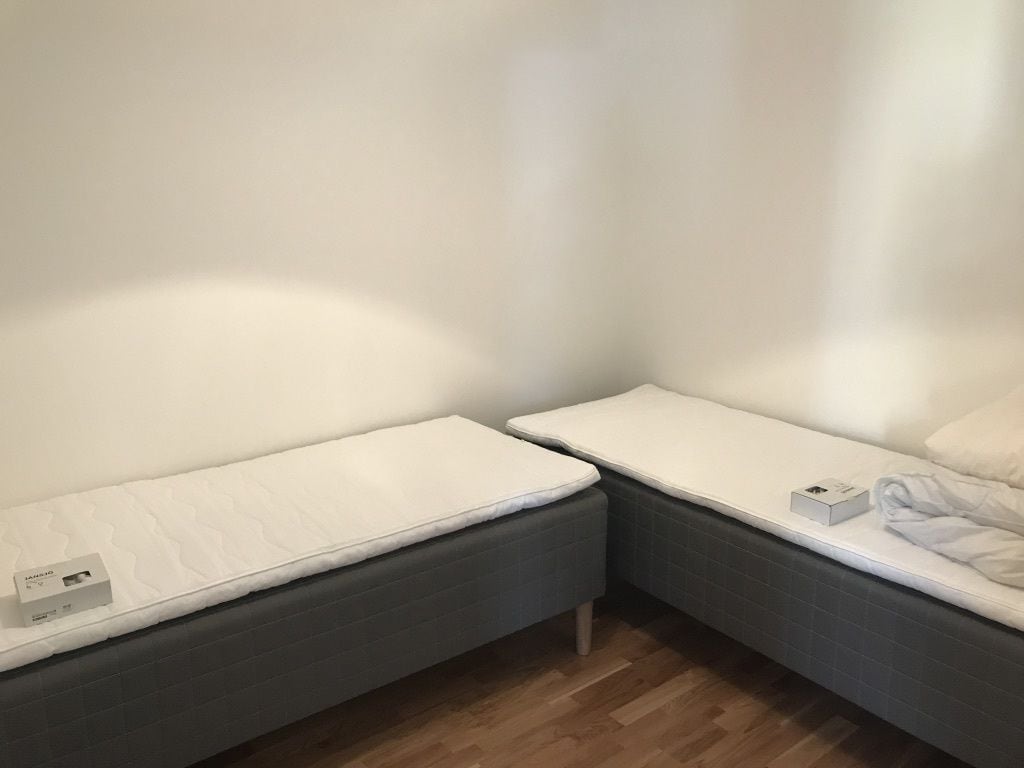 A corner bedroom with two single beds, each with a white mattress and matching pillows.