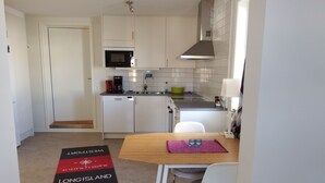 A compact kitchen with white cabinets, a microwave, a coffee maker, and a sink. There's a dining table with two chairs and a rug with text on it. - Sjöhuset (Ellos)