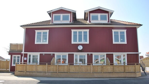 A two-story building with a red exterior and white trim, featuring multiple windows and a wooden deck in front. - Sjöhuset (Ellos)