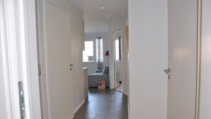 A hallway with white doors, a grey sofa, and a window with curtains. - Sjöhuset (Ellos)