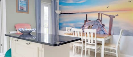 A dining area with a view of a sunset over water, a white table with chairs, and a small island with a bowl.