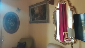 Una sala de estar con un sofá, un sillón, un televisor, un espejo decorativo y un aire acondicionado instalado en la pared.