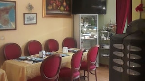 Un comedor con una mesa dispuesta para seis personas, rodeada de sillas rojas. Un candelabro cuelga del techo y un televisor está montado en la pared.