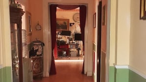 Un pasillo con una araña, un espejo y una puerta que da a una habitación con un escritorio y una silla.