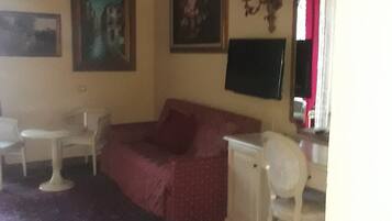 A room with a sofa, a small table, a chair, a TV, and a painting on the wall.