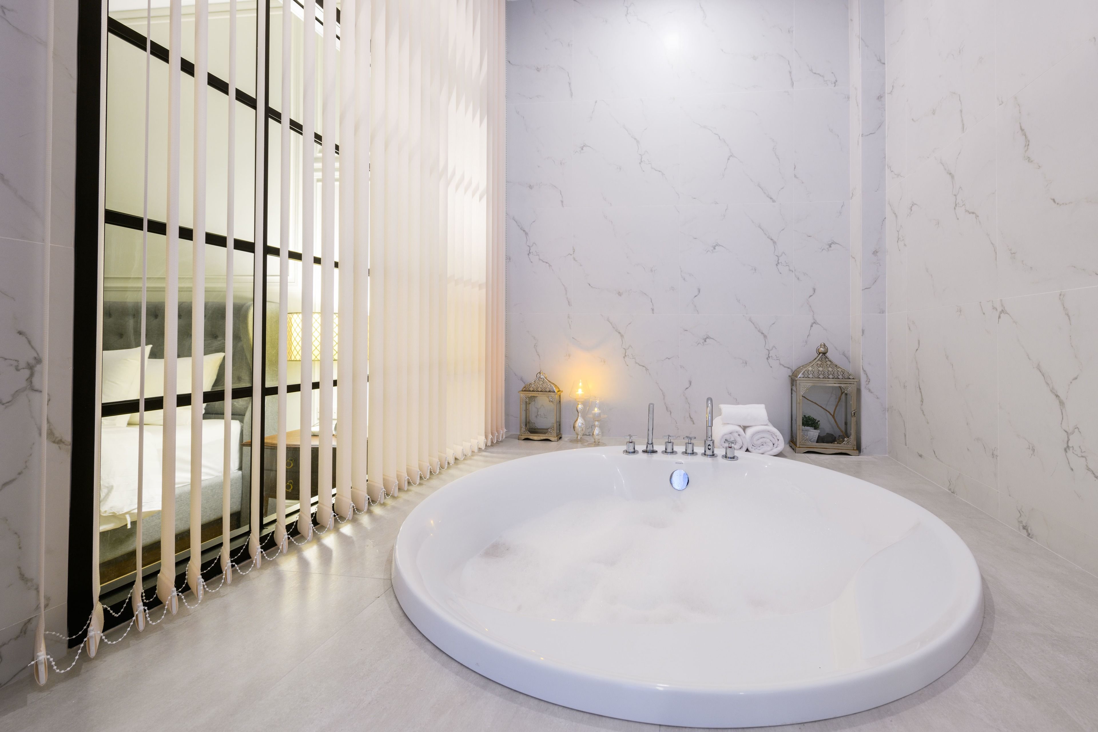 A modern bathroom with a large oval bathtub, a glass partition, and marble walls.