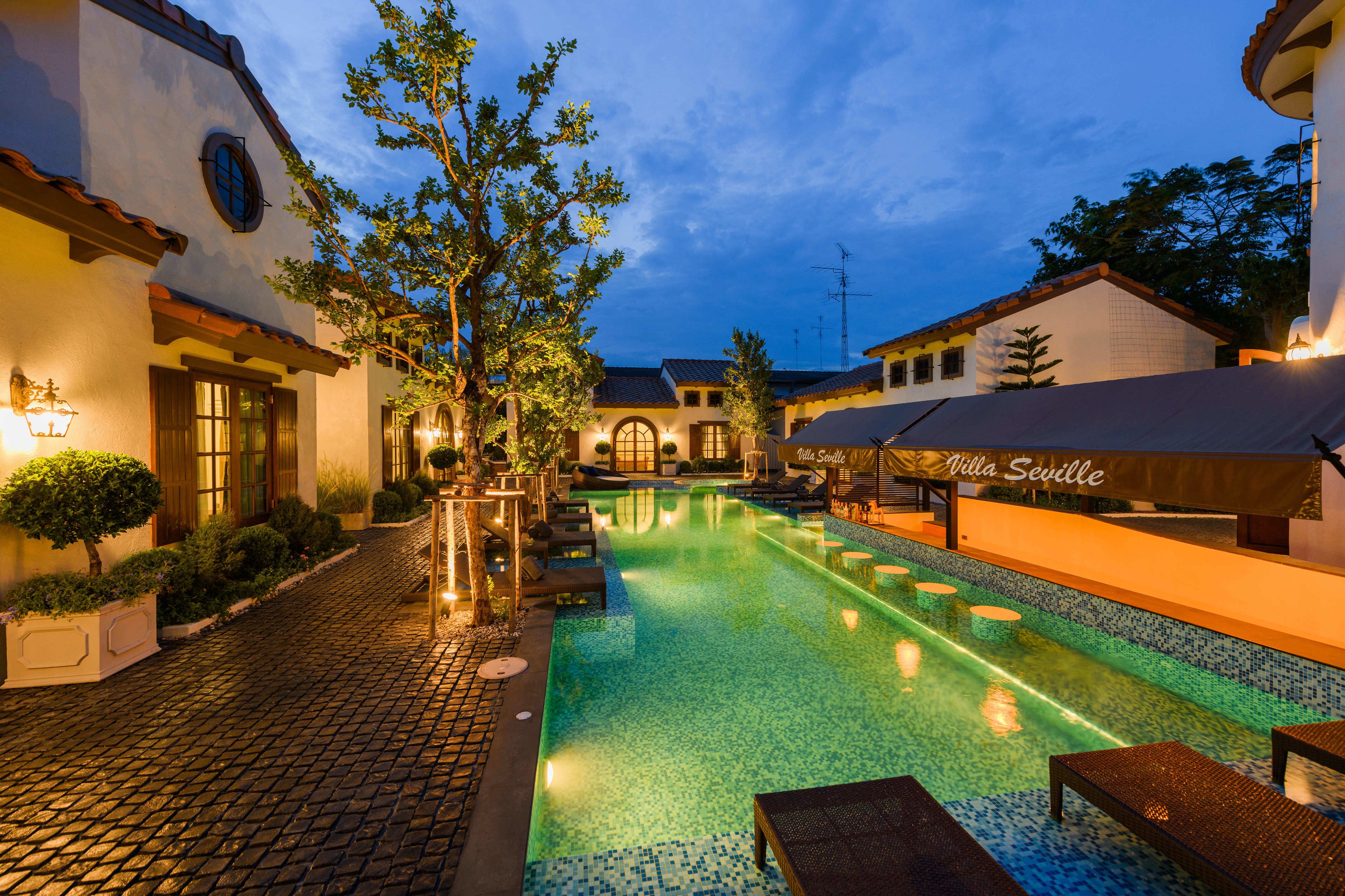 Un patio con piscina, sillas de descanso y un restaurante llamado "Villa Seville".