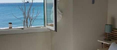 A hotel room with a large window, a bed, a bedside table, and a wall-mounted shelf with toiletries.