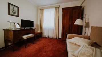 A hotel room with a wooden desk, a television, a sofa, and a large window with curtains.
