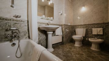 Een badkamer met een bad, een wastafel op een zuil, een toilet en een bidet.
