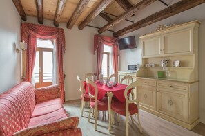 A dining area with a red tablecloth, wooden chairs, a sofa, and a cream-colored cabinet with a television above it. - Venezia - Santa Croce 1797 (Venice)