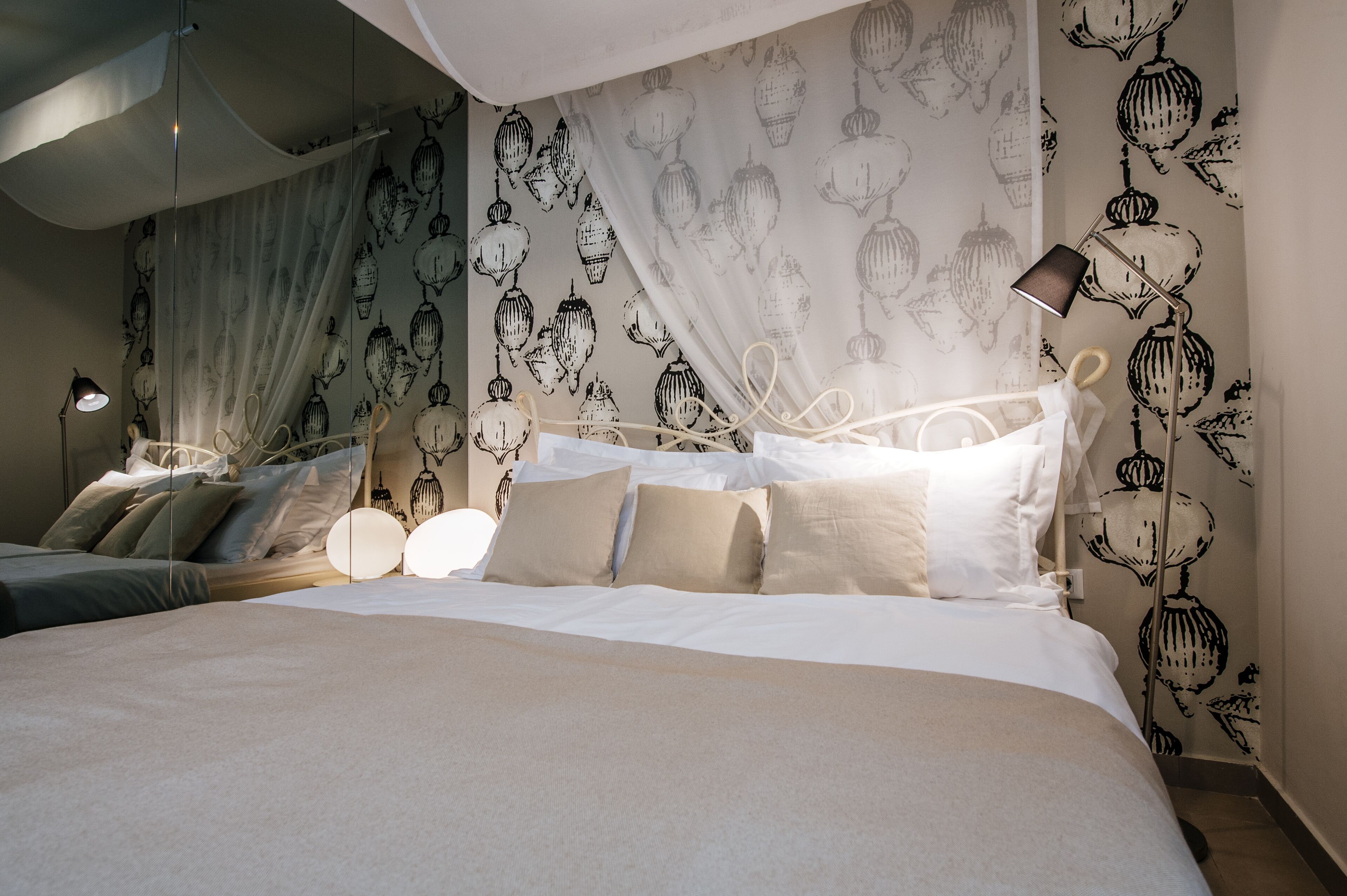 A neatly made bed with a canopy, a bedside lamp, and a wall with a decorative pattern.