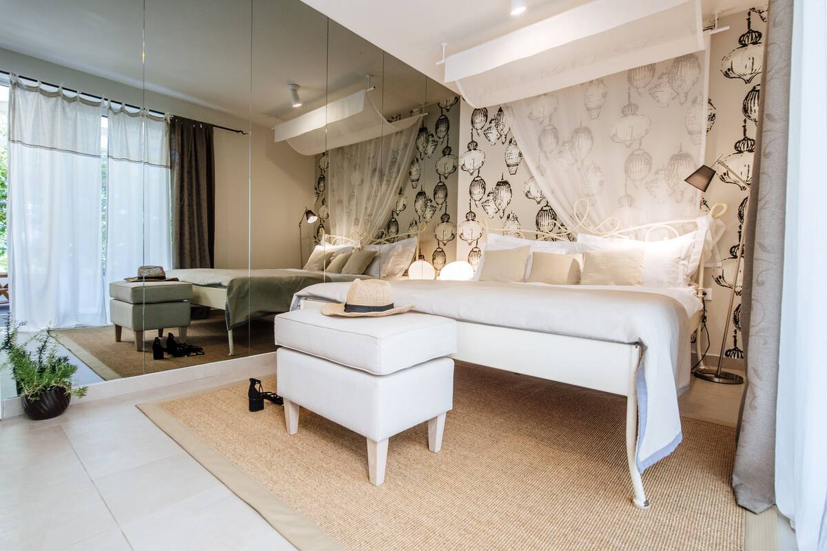 A modern bedroom with a large bed, a nightstand, a mirror, and a potted plant.