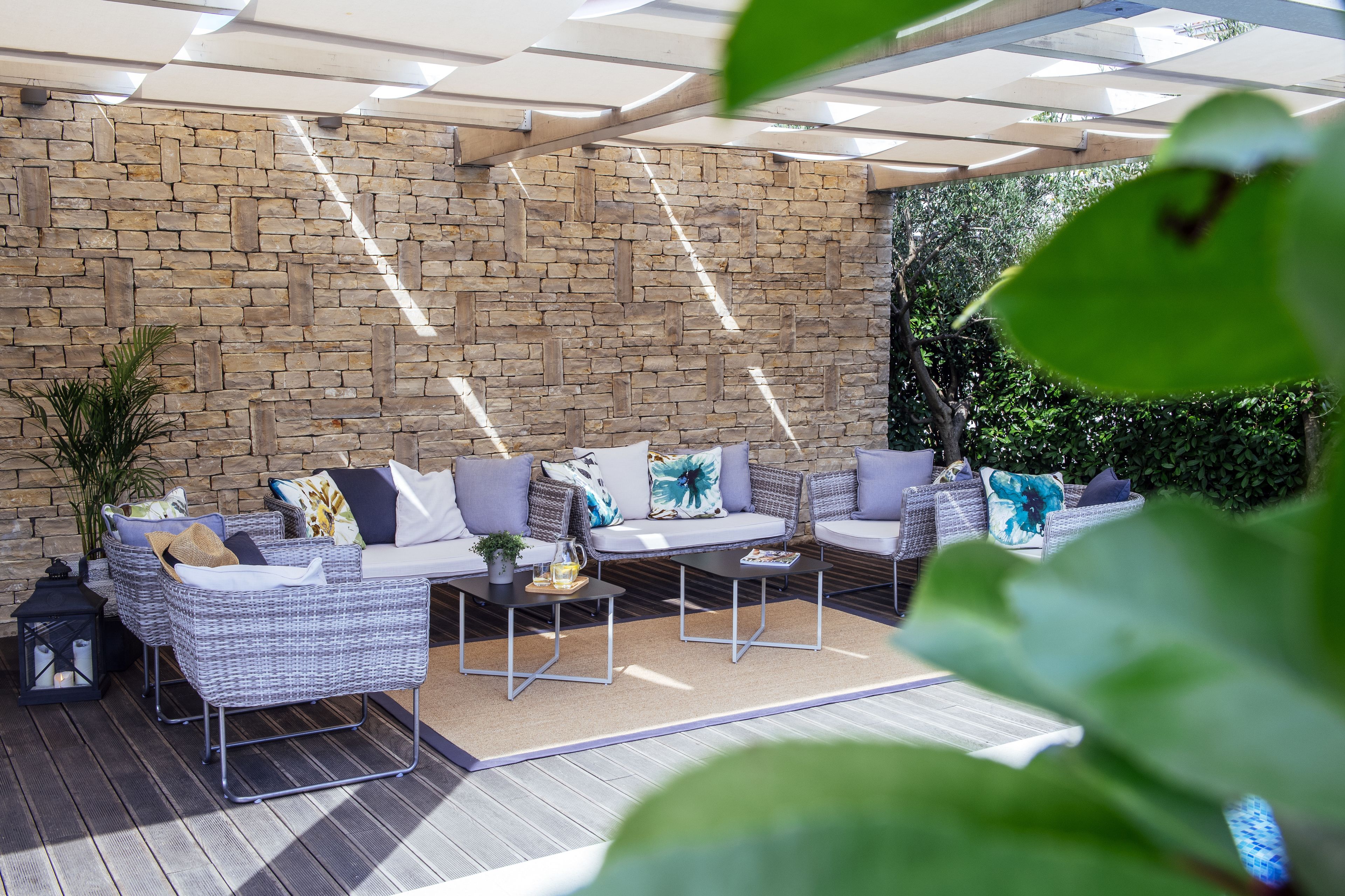 An outdoor patio with wicker furniture, a stone wall, and a ceiling with natural light.