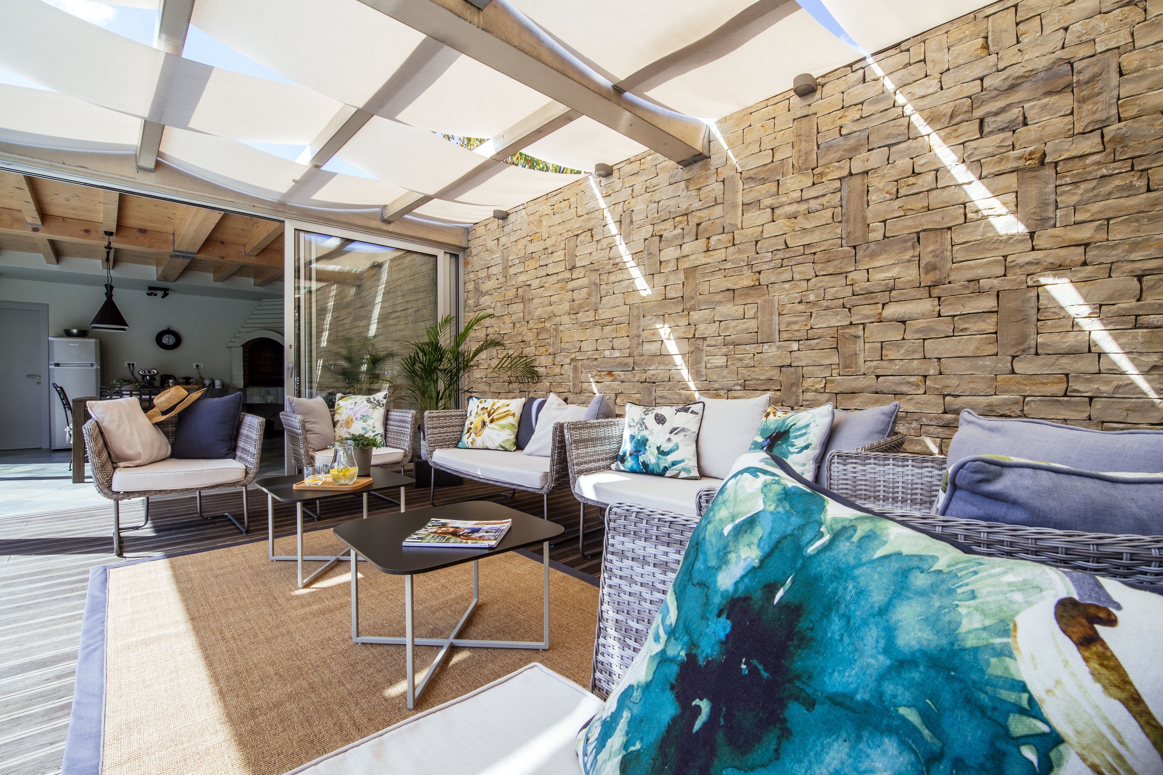 A modern outdoor seating area with wicker furniture, a stone wall, and a glass door leading to an interior space.
