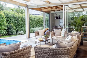 A modern outdoor living area with wicker furniture, a pool, and a glass door leading to a kitchen. - Villa Mirakul (Sukosan)
