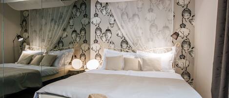 A modern hotel room with two beds, a large mirror, and a decorative hat on the bed.
