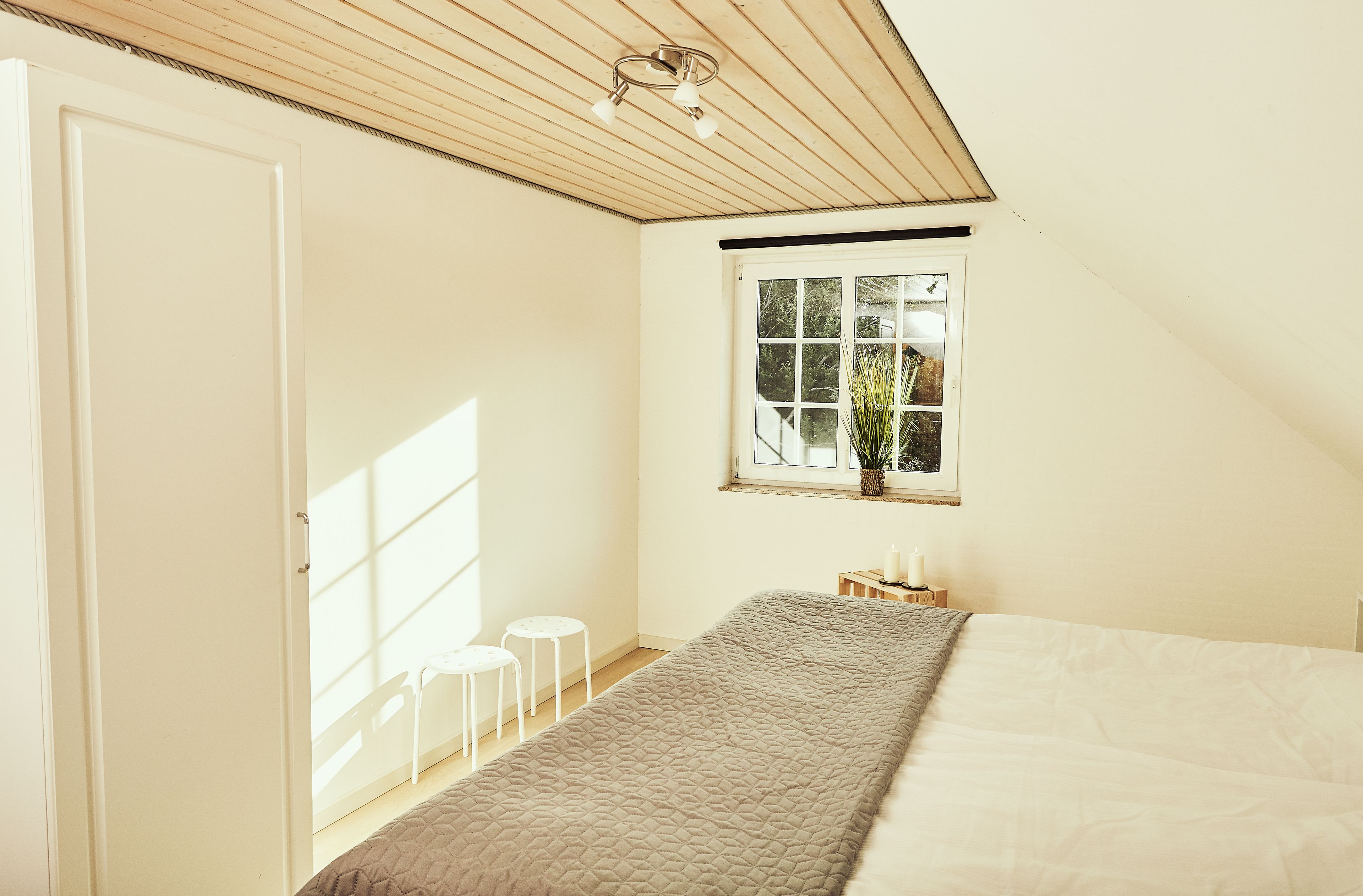 Een slaapkamer met een bed, een raam met uitzicht, een deur en een kleine tafel met een plant.
