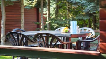 An outdoor dining area with a table and chairs, surrounded by trees and a wooden fence.