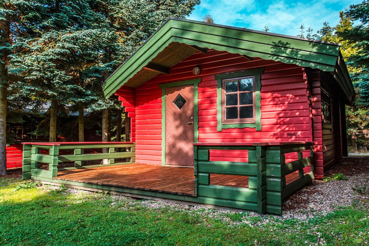 Eine kleine, rote Holzhütte mit einer grünen Veranda und einer Holzterrasse.
