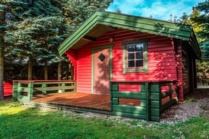 Una piccola baita di legno rossa con un portico verde e un'area esterna in legno.
