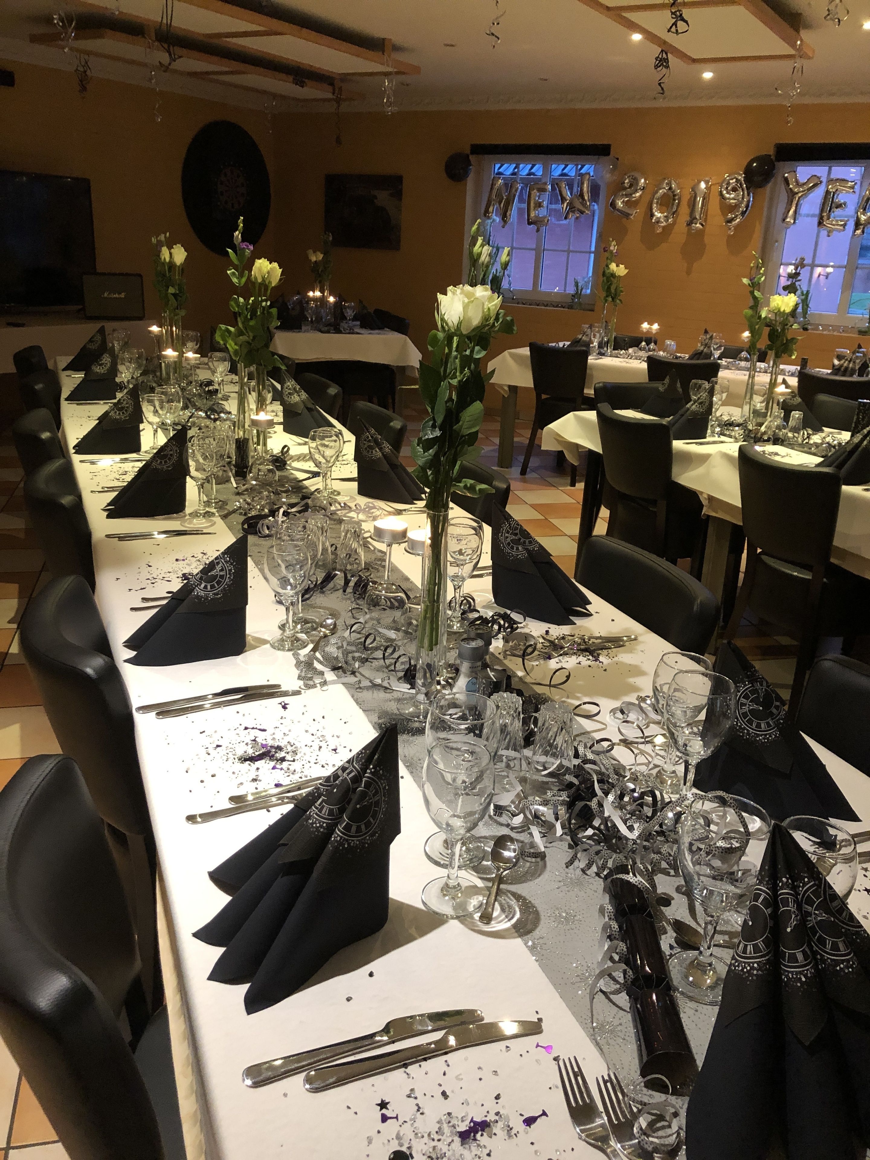 Una larga mesa de comedor dispuesta para un evento formal, con múltiples puestos de bienvenida, copas y cubiertos.